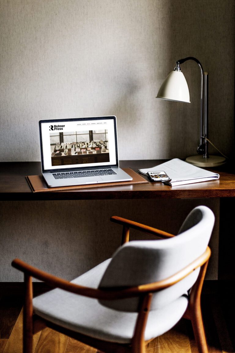 Home office desk with a laptop displaying the Rohner Press website, showcasing WordPress design and development by Matt Snyder at A LA MODE designs, an award-winning web developer.