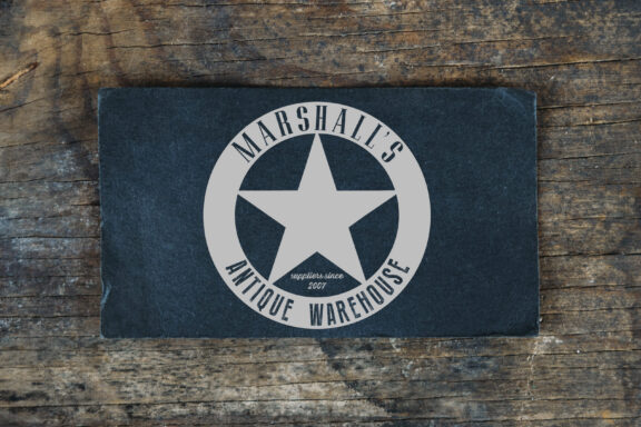 Marshall’s Antique Warehouse circular logo with a large star in the center and small text “suppliers since 2007,” shown on a dark card on a rustic wood surface. Brand identity services by Rebecca Snyder.