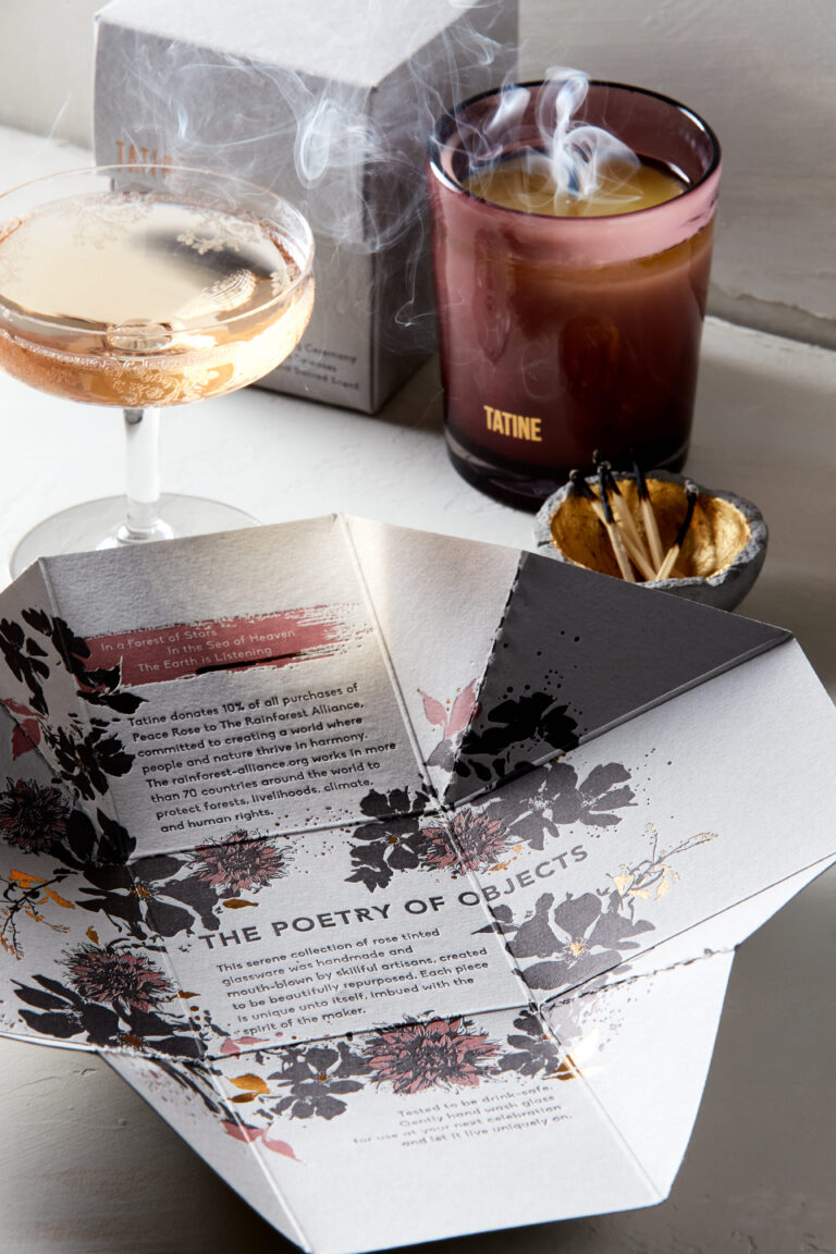 TATINE candle beside a coupe glass and match bowl, with folded floral ‘Peace Rose’ packaging in the foreground (package design by Rebecca Snyder, A LA MODE designs).