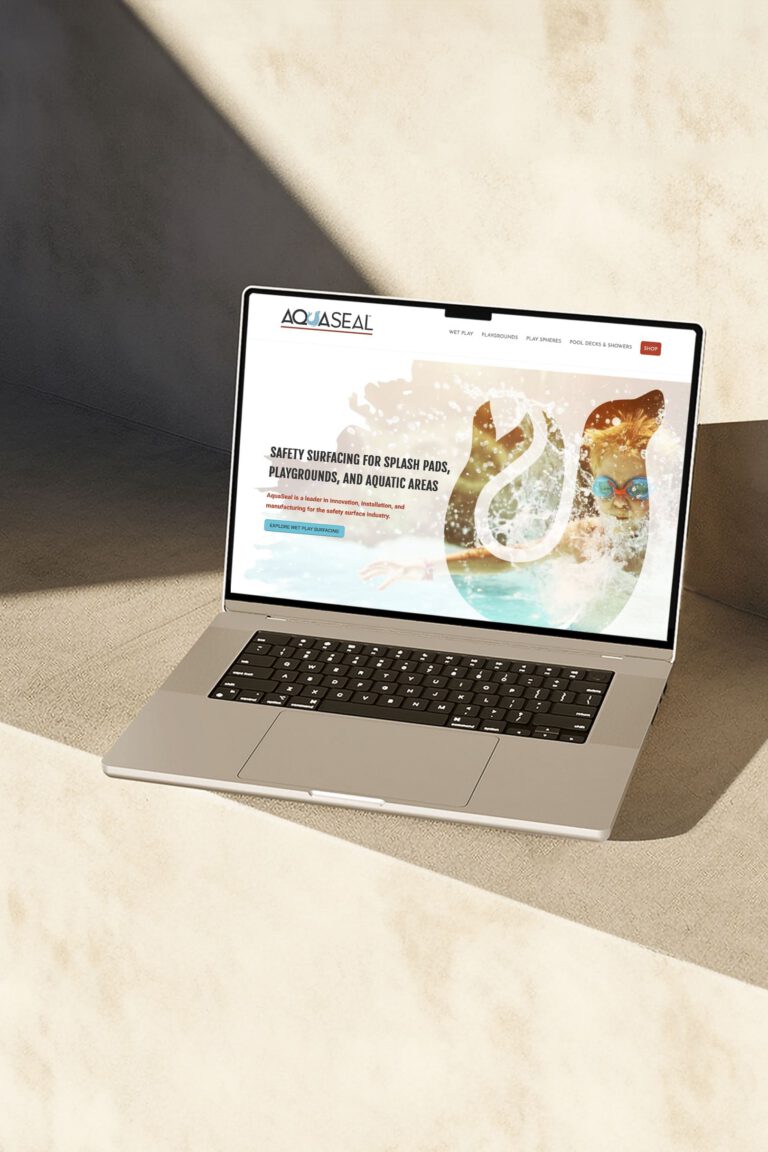 Silver laptop on a sunlit surface displaying the AquaSeal homepage with a water-surfacing hero graphic; showcasing website design and development by Matt Snyder at A LA MODE designs, an award-winning web developer.